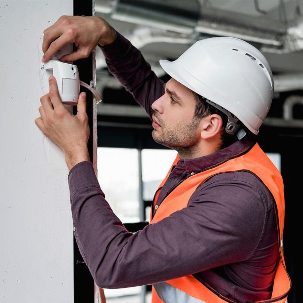 Man in uniform and helmet checking fire alarm device.
